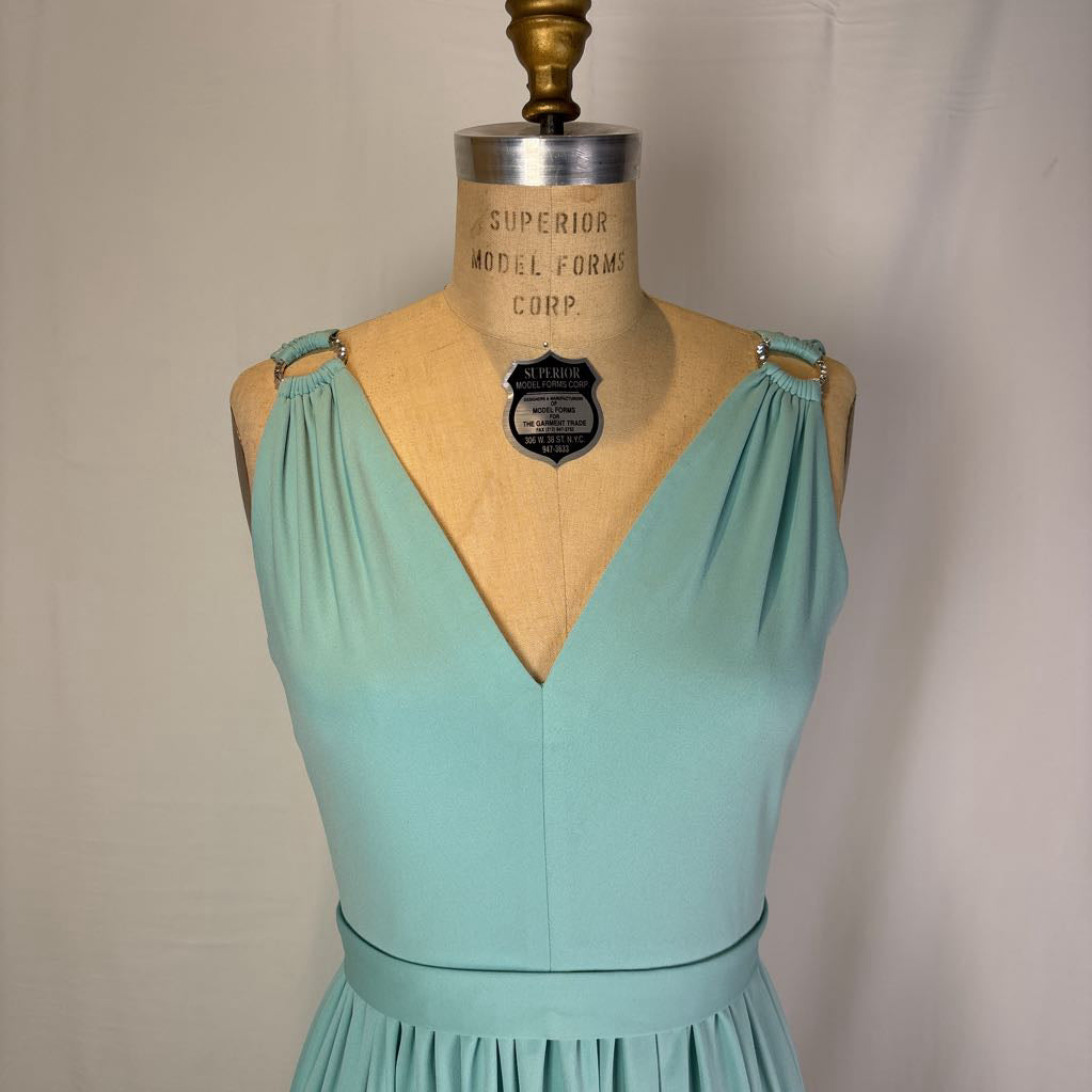 A mint green sleeveless dress displayed on a vintage wooden dress form mannequin against a neutral off-white background.