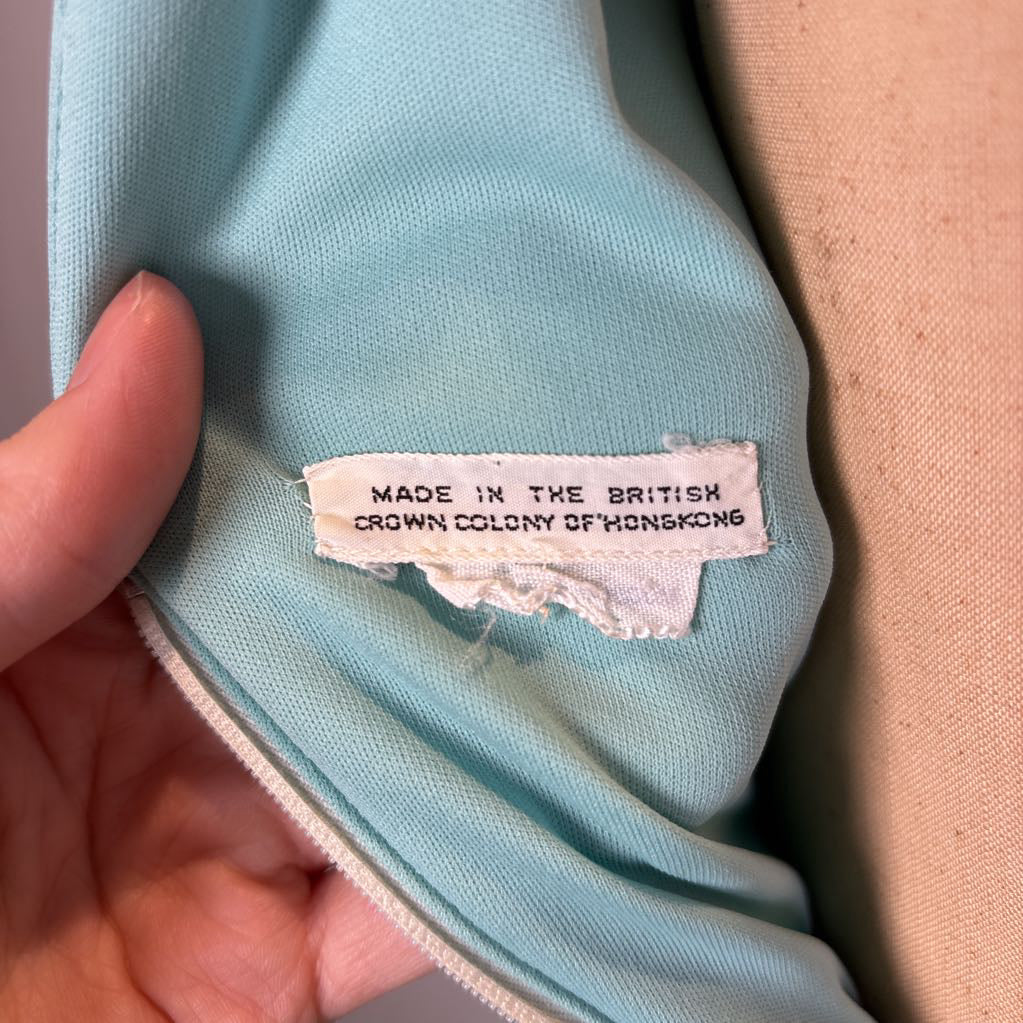 A close-up of a light blue fabric interior with a hand holding it open to reveal a sewn-in label that reads 'MADE IN THE BRITISH CROWN COLONY OF HONGKONG.'.