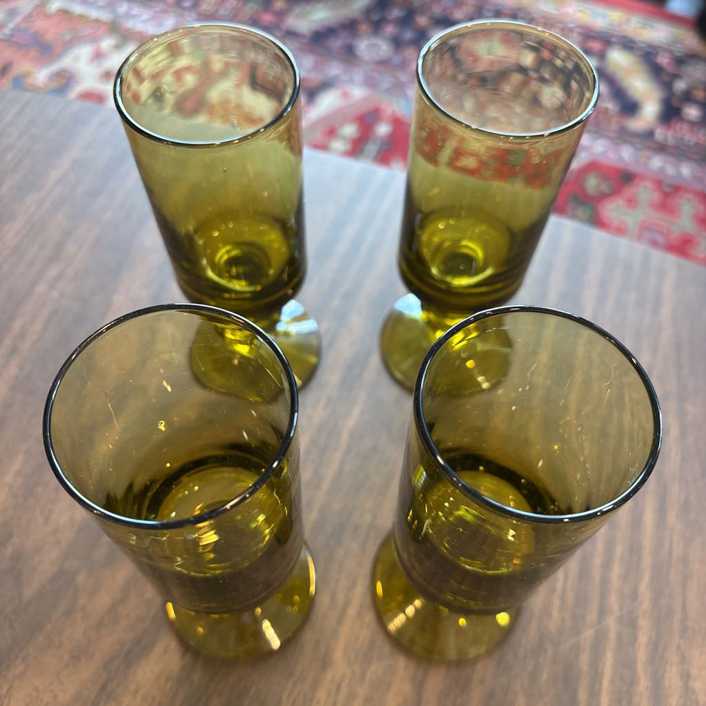 Four vintage glass tumblers arranged in a square on a wooden tabletop, with a patterned rug visible in the background.