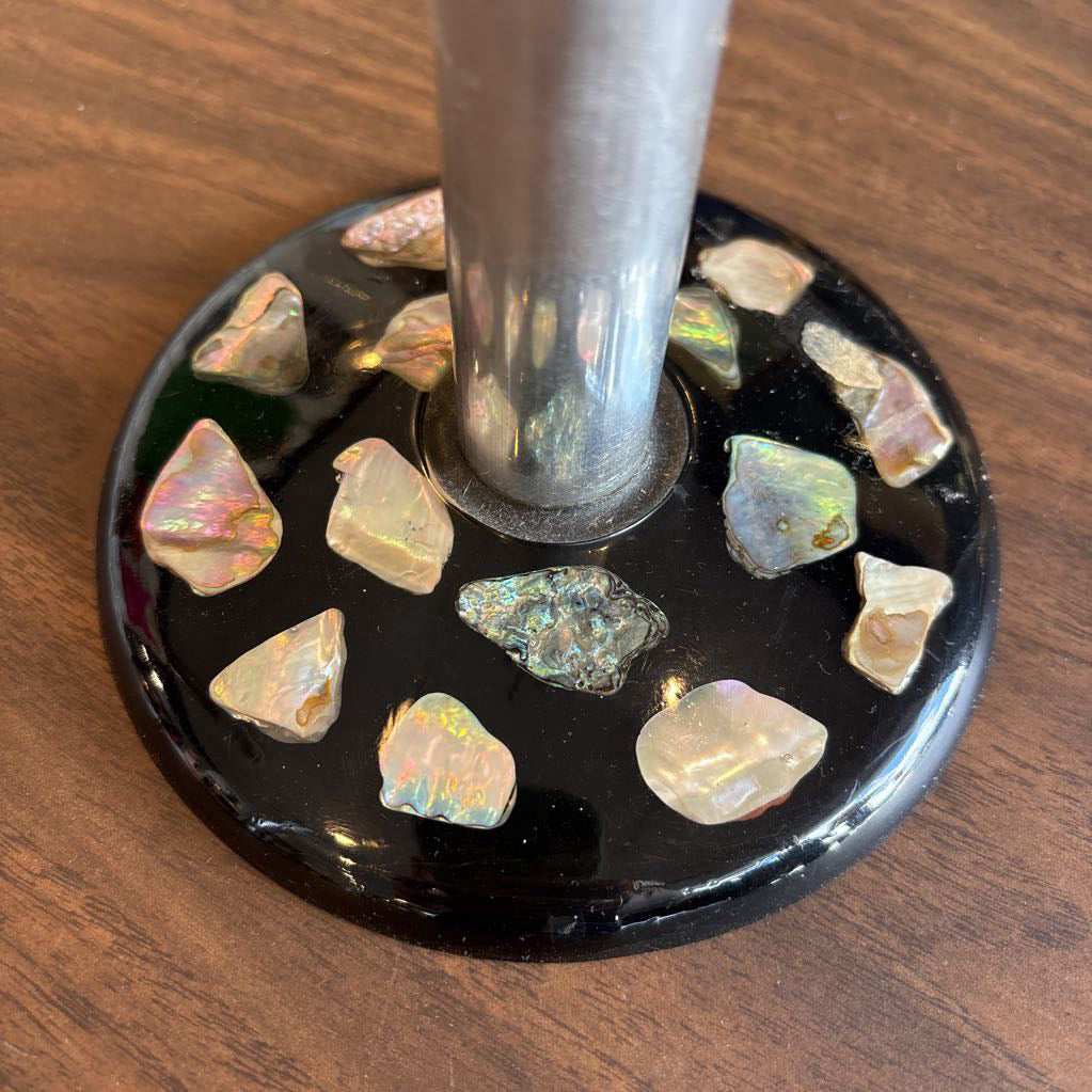 A close-up of a black circular base with embedded iridescent opal-like stones, supporting a metallic silver pole on a wooden surface.