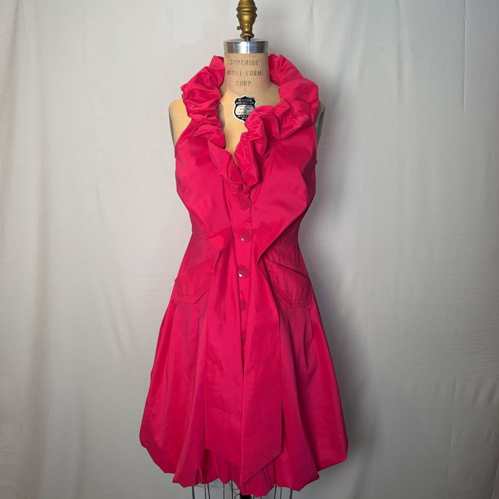 A bright pink button-up sleeveless dress with a ruffle collar on a mannequin in front of a white wall.