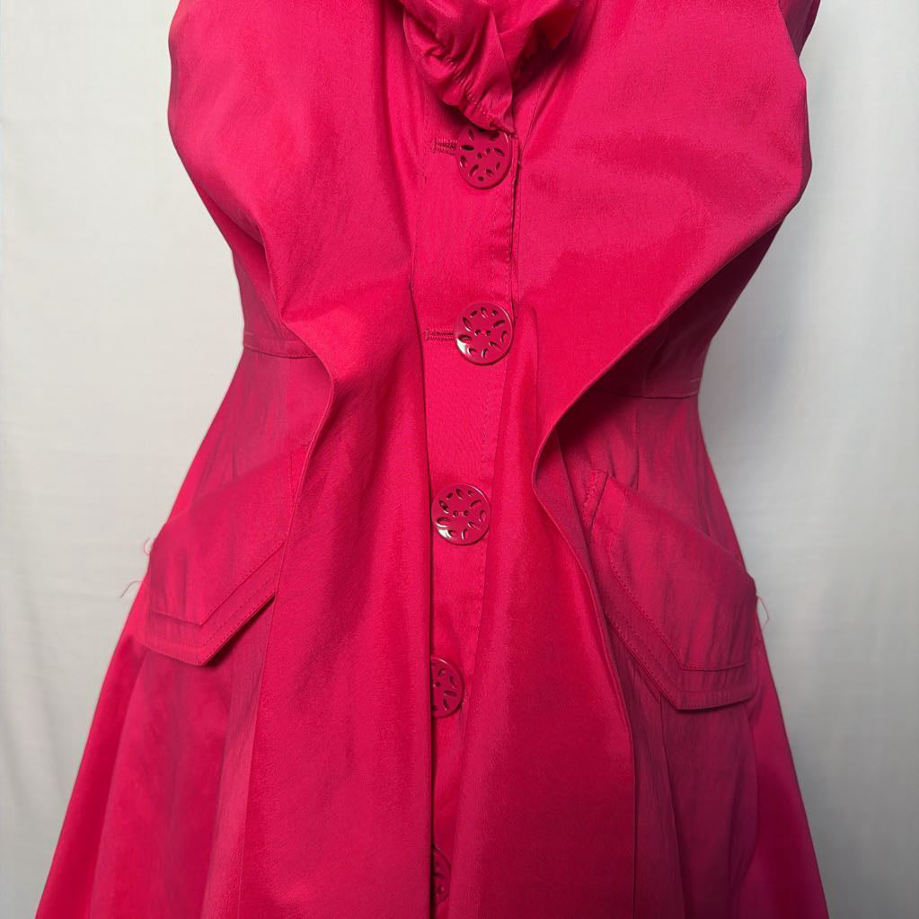 A bright pink button-up sleeveless dress with a ruffle collar on a mannequin in front of a white wall.