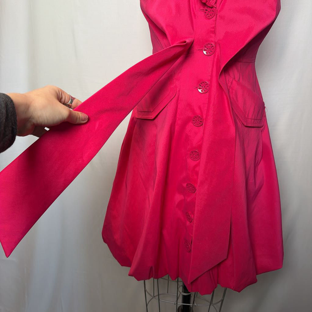 A bright pink button-up sleeveless dress with a ruffle collar on a mannequin in front of a white wall.