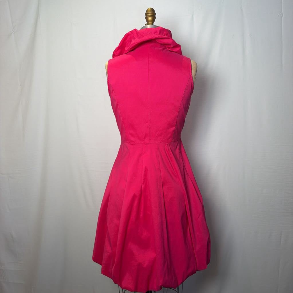 A bright pink button-up sleeveless dress with a ruffle collar on a mannequin in front of a white wall.