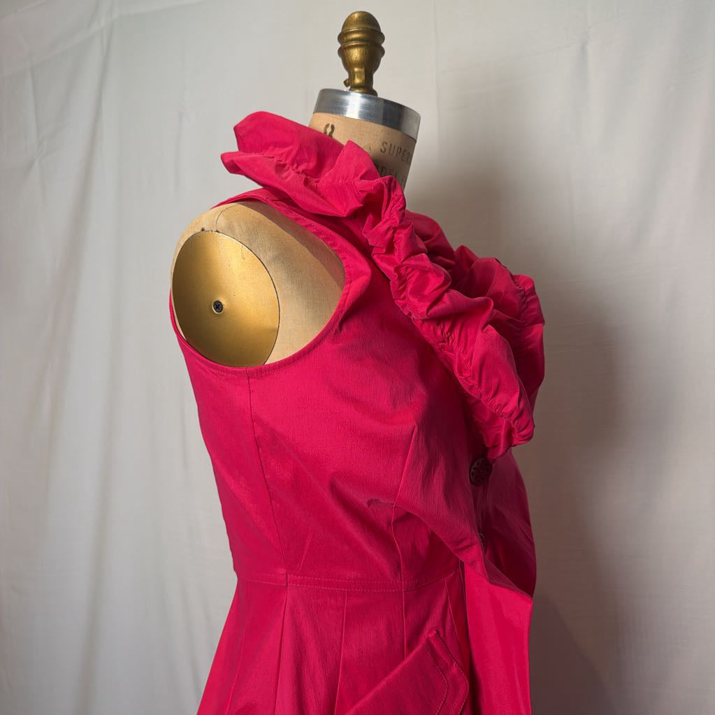 A bright pink button-up sleeveless dress with a ruffle collar on a mannequin in front of a white wall.