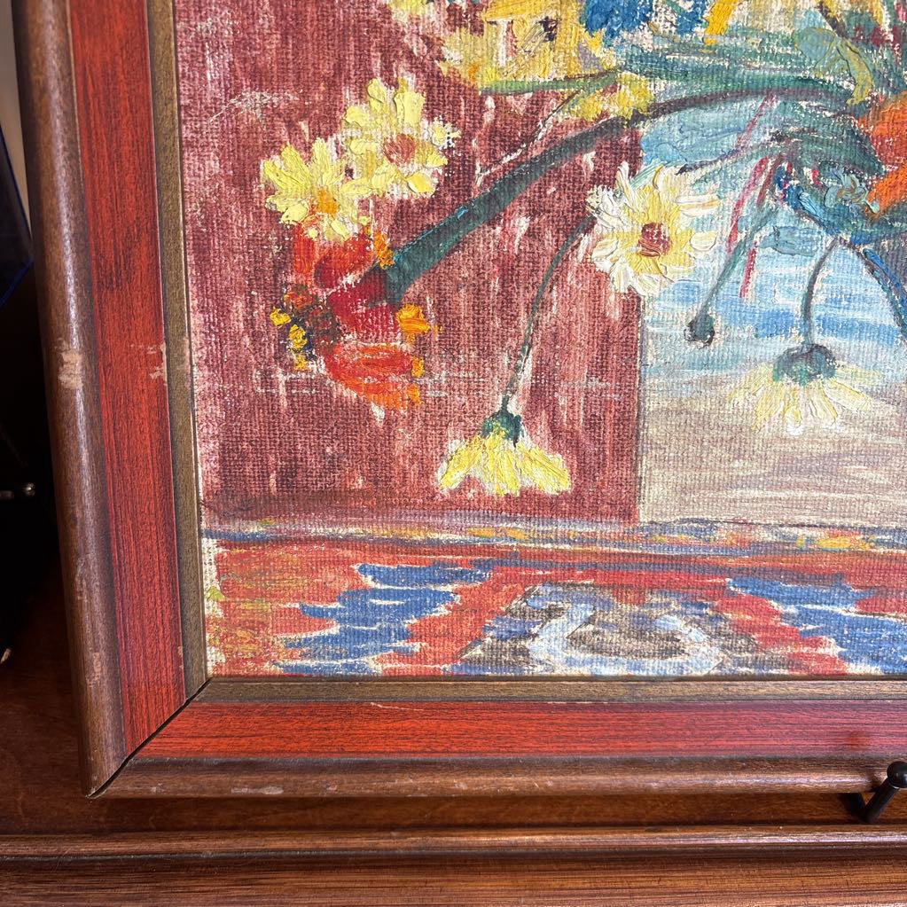 A framed still life of flowers in a vase on a wooden surface.
