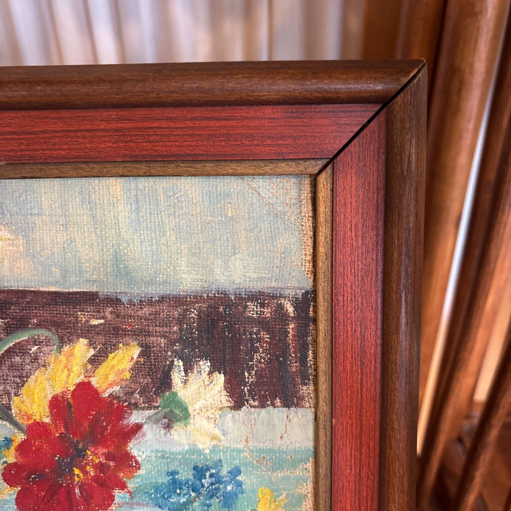 A framed still life of flowers in a vase on a wooden surface.
