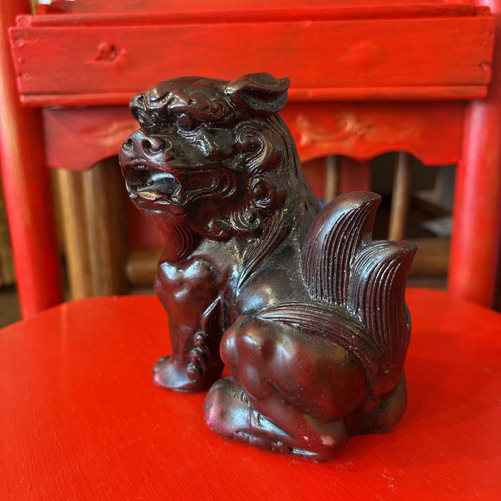 Mahogany colored foo dog figurine on a red surface.