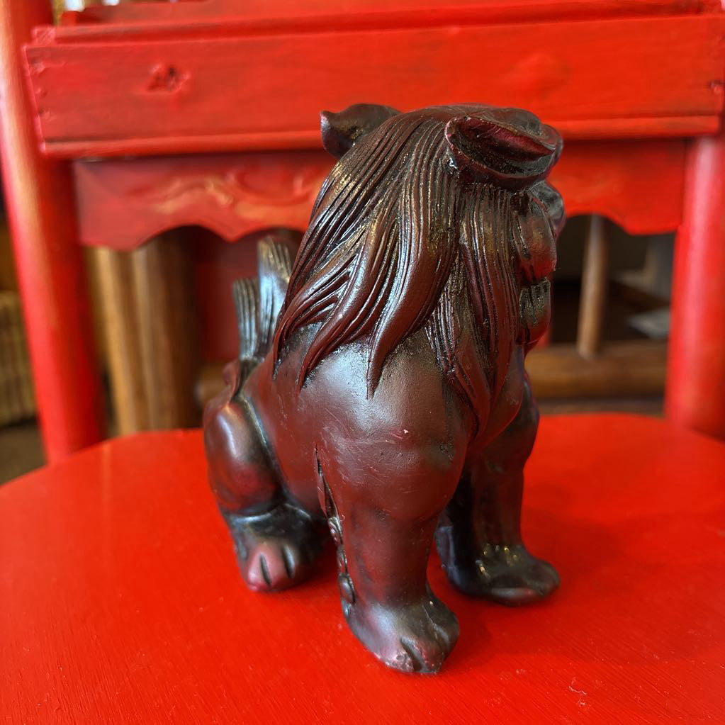 Mahogany colored foo dog figurine on a red surface.
