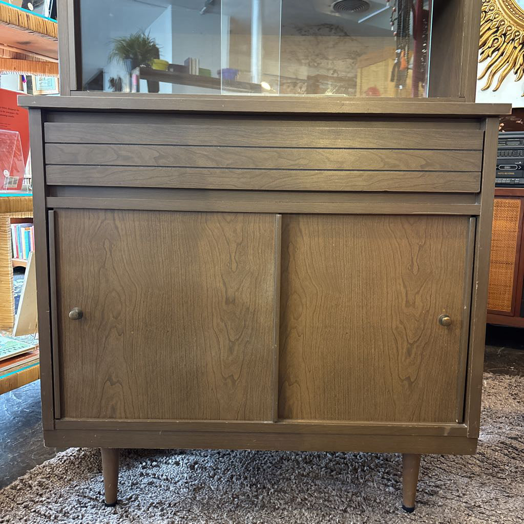 A large wooden hutch with two sliding wooden doors. The cabinet is in a store setting.