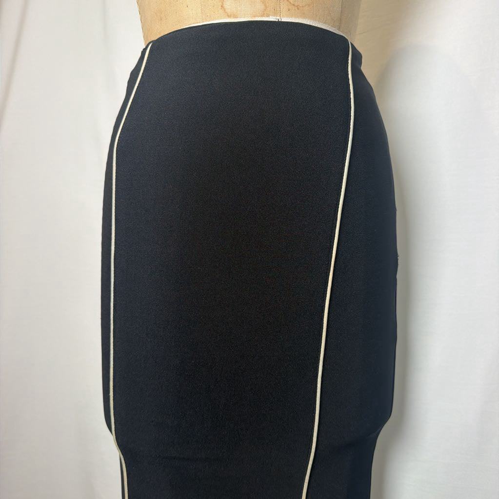 A black pencil skirt with white lines down the front and side on an antique mannequin in front of a white fabric wall.