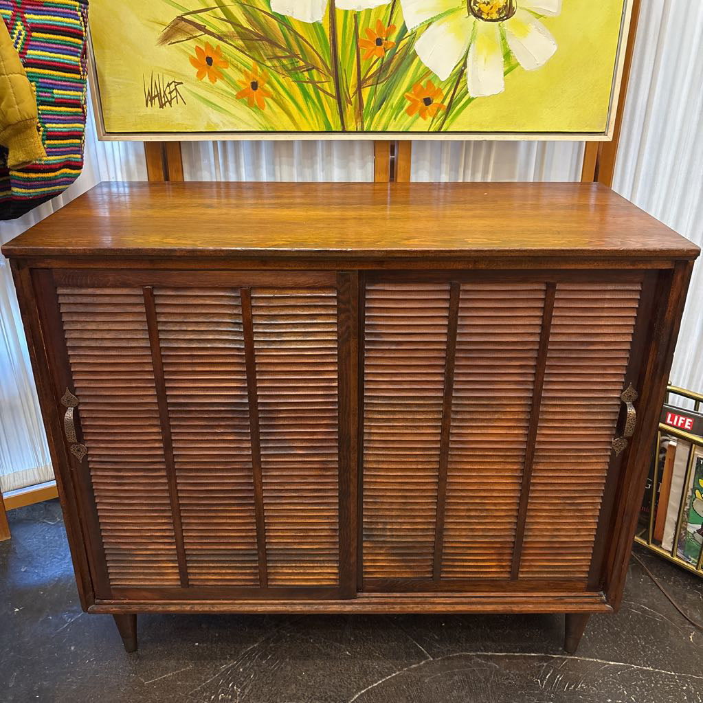 A brown wooden cabinet with sliding doors in a room setting.