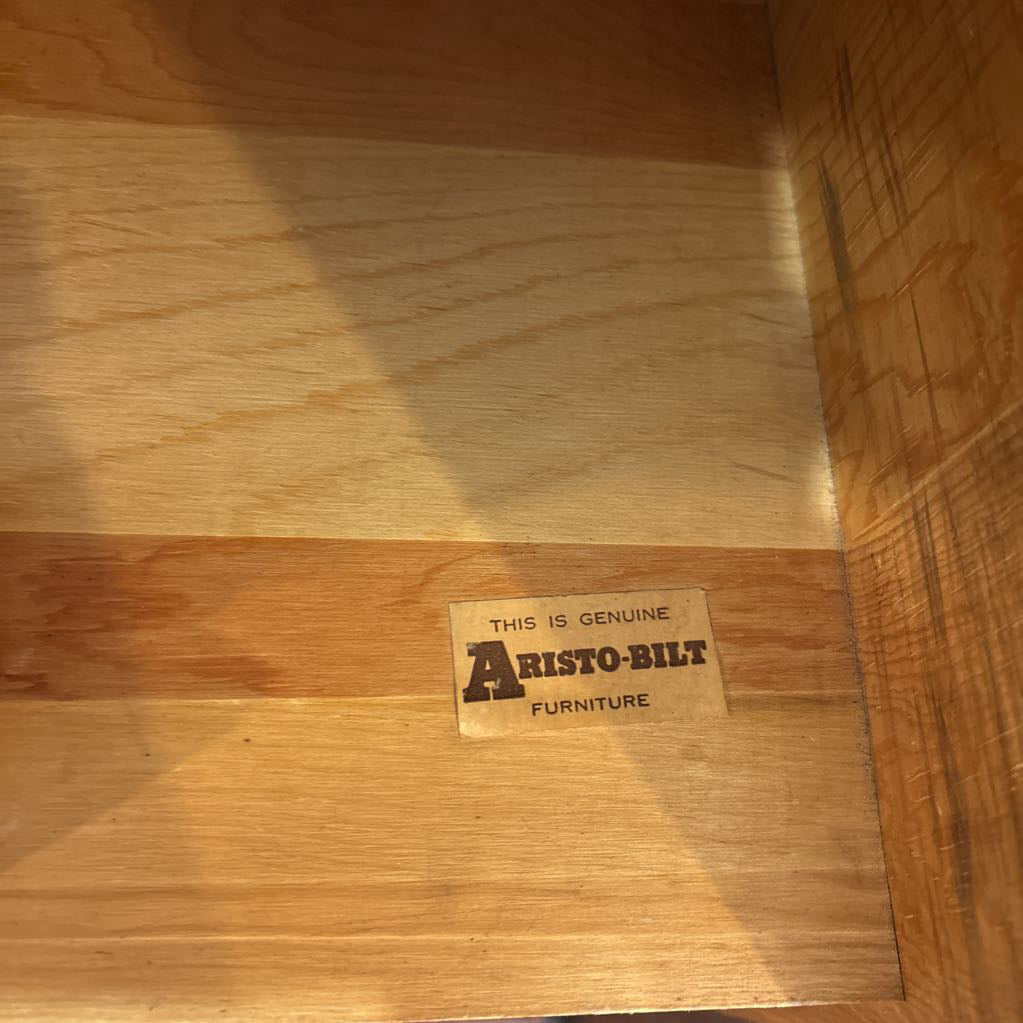 The interior of a wooden shelf with a sticker reading 'THIS IS GENUINE ARISTO-BILT FURNITURE.'