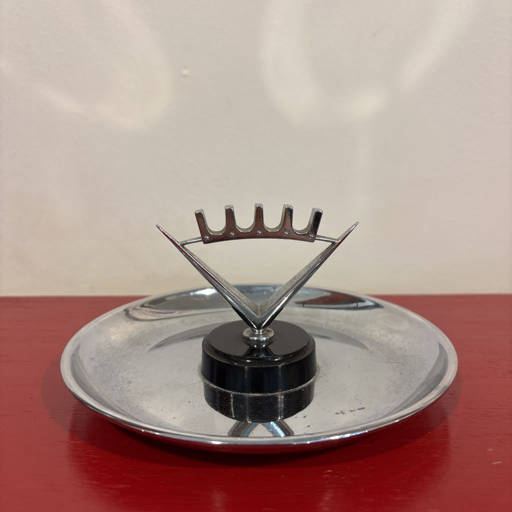 A mid-century style chrome ashtray dish on a red surface and up against a white wall.