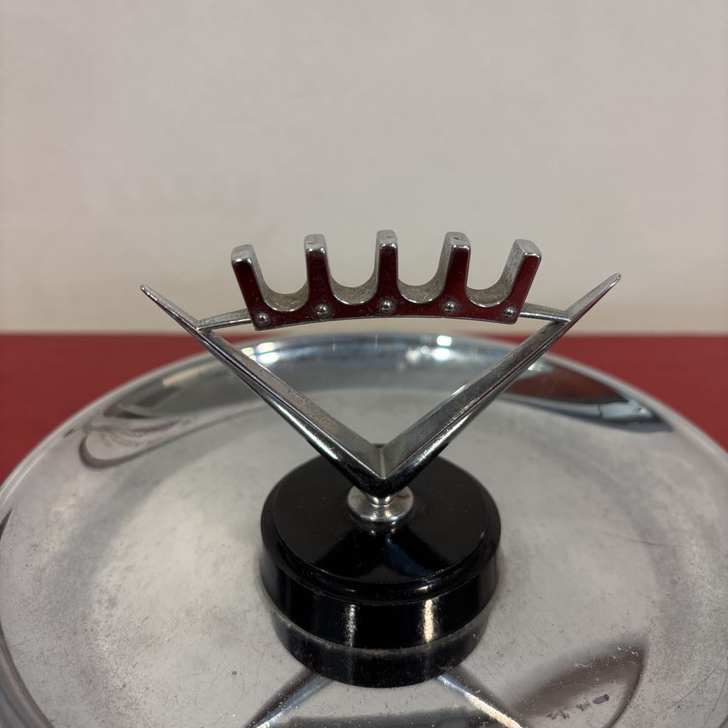 A mid-century style chrome ashtray dish on a red surface and up against a white wall.