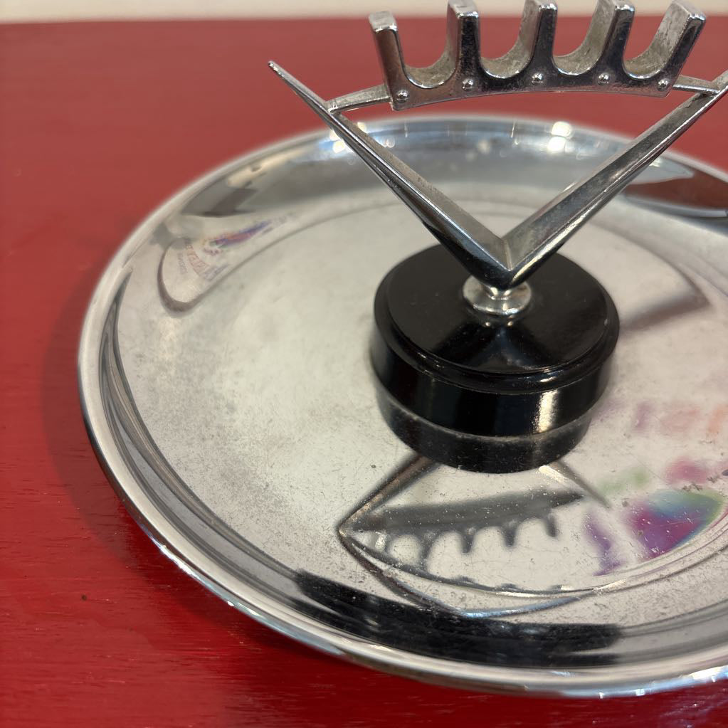 A mid-century style chrome ashtray dish on a red surface and up against a white wall.