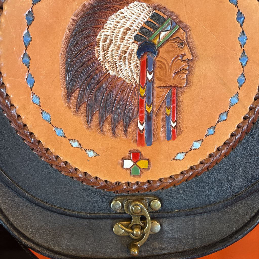 A black leather belt bag with a Native American figure's profile embossed in a circular design on the front. This bag sits on an orange cushion.