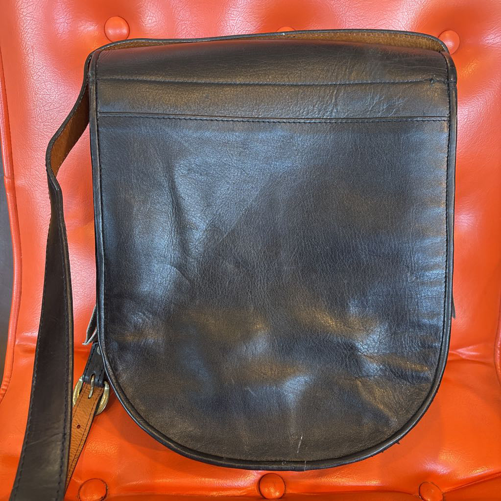 A black leather belt bag on an orange cushion in a room setting.