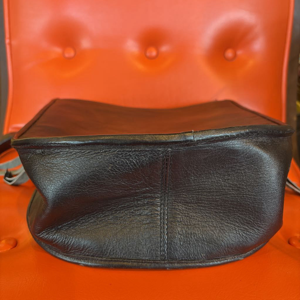 A black leather belt bag on an orange cushion in a room setting.