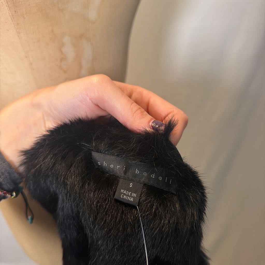 A hand holding a brand tag inside a fur vest that reads "Sheri Bodell"