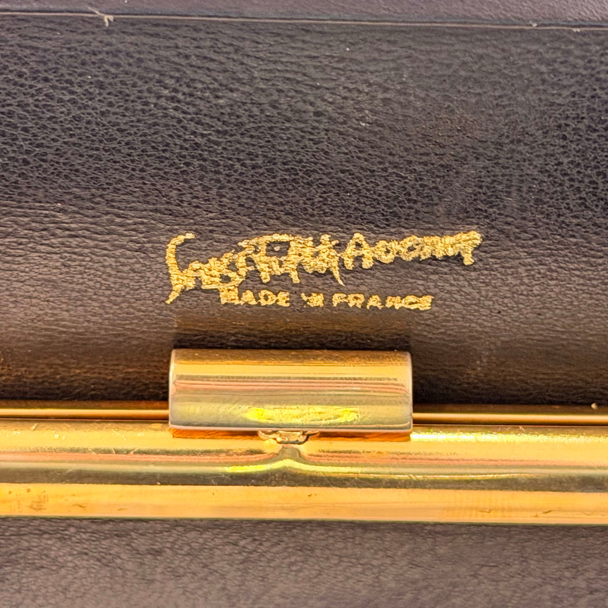 Close-up of a dark brown textured leather interior with gold-tone metal hardware and a gold embossed signature reading 'Saint Laurent' and 'MADE IN FRANCE'.