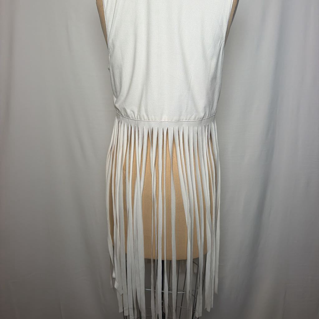 A white vest with long fringe on an antique mannequin in front of a white fabric wall.