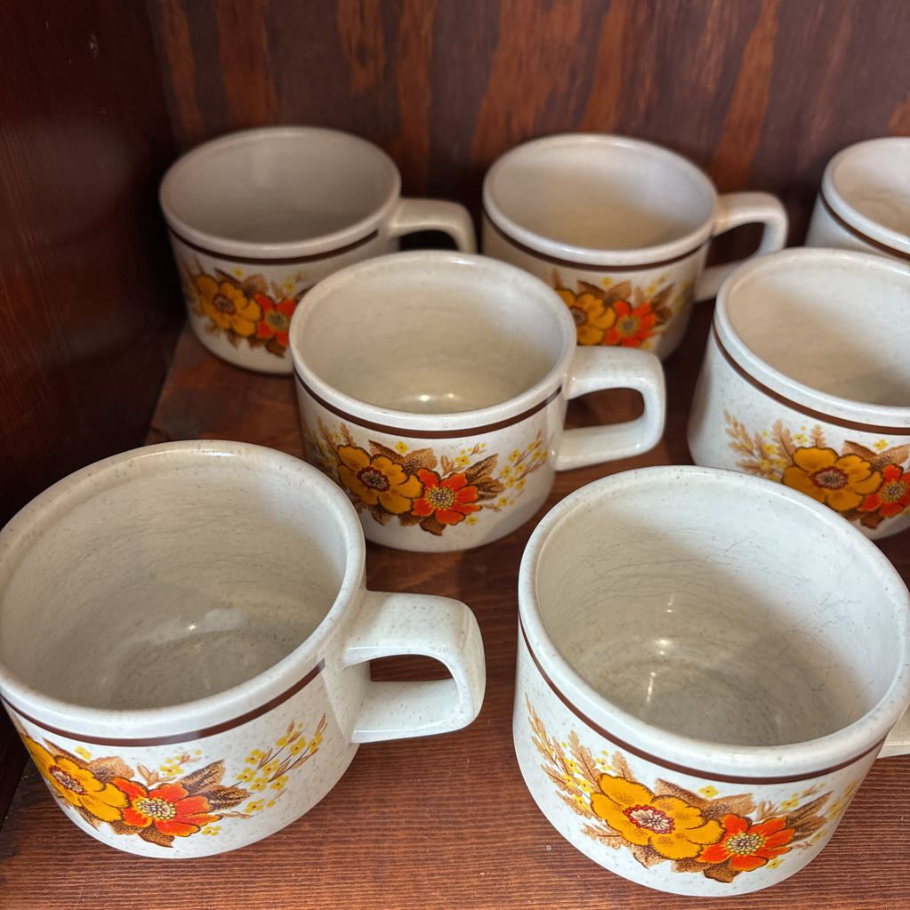 White ceramic mugs with floral designs in a wooden cabinet.