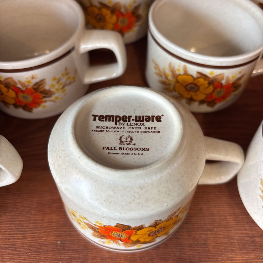 White ceramic mugs with floral designs in a wooden cabinet.