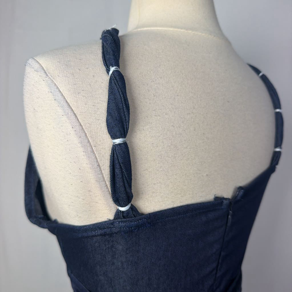 Close-up back view of a dark navy blue garment displayed on a cream mannequin torso, featuring a braided shoulder strap detail with white elastic loops.