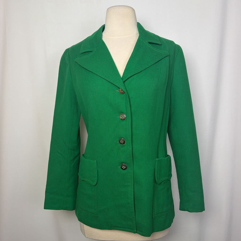 A bright green women's blazer jacket with notched lapels, a three-button front closure, and two front patch pockets, displayed on a cream-colored dress form against a white fabric backdrop.