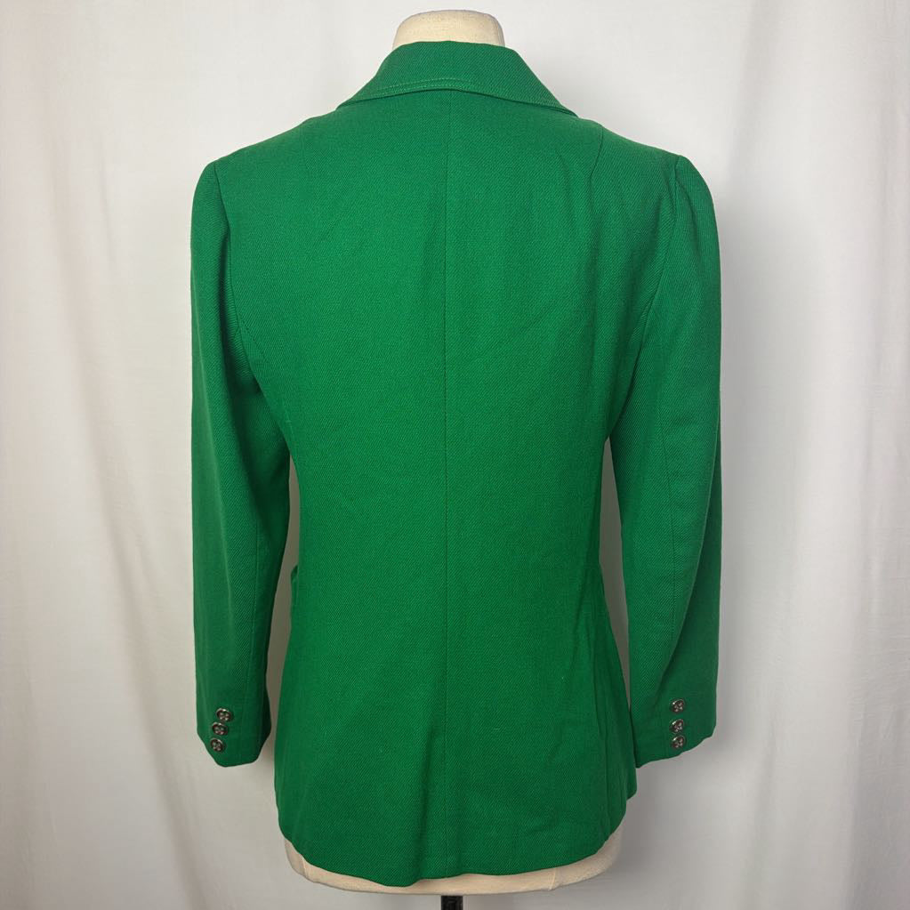 A bright green women's blazer shown from the back on a cream dress form against a white fabric backdrop.