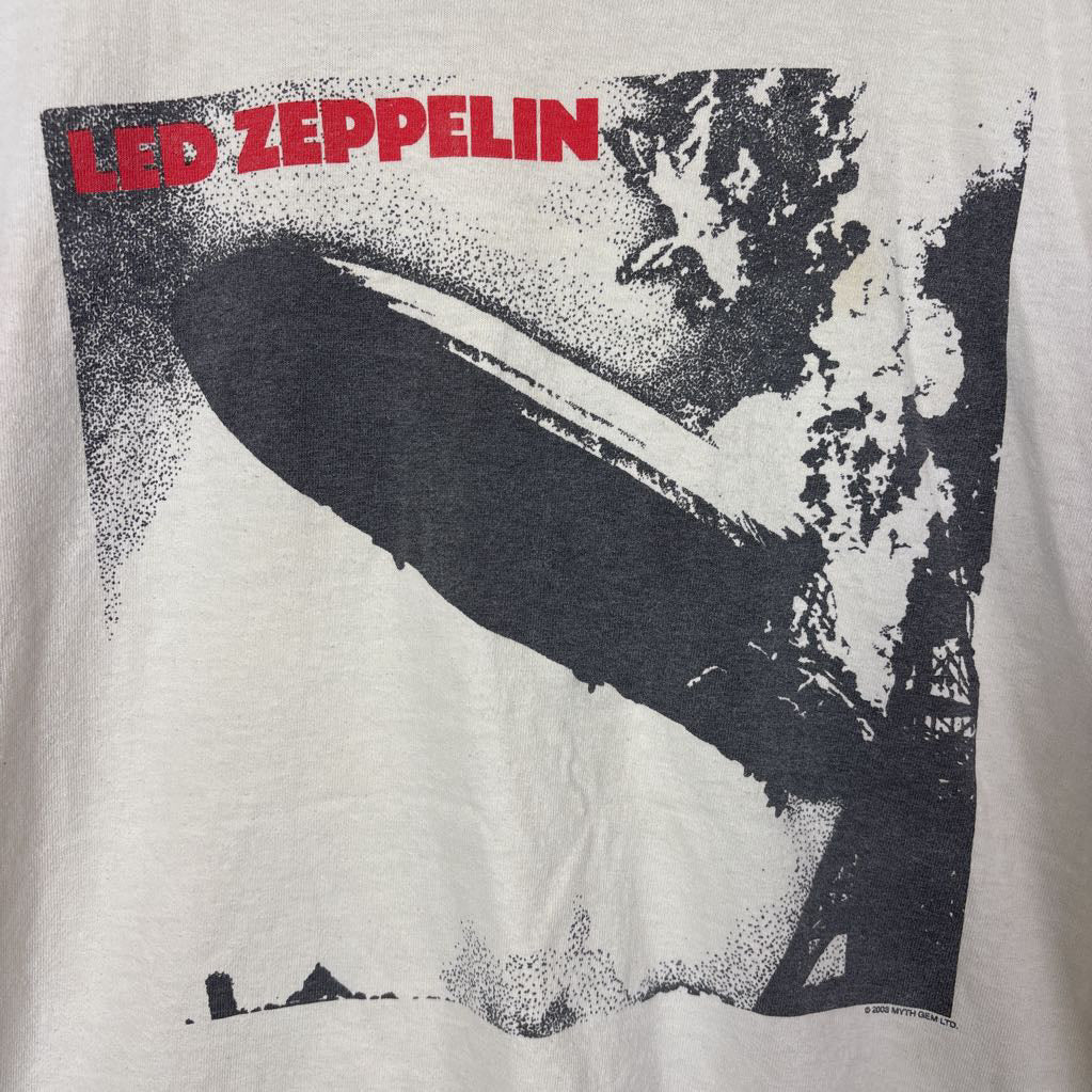 A white vintage style short sleeve t-shirt with an image of a Led Zeppelin album cover and the band's name in red letters. The shirt hangs on a wooden rack against a white background.