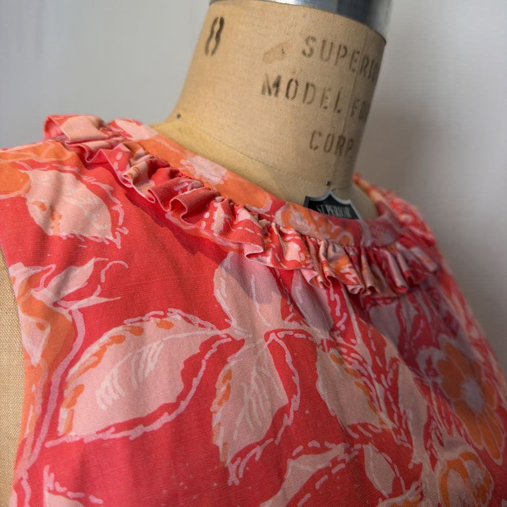 A pink & peach floral mod dress on a dress form in front of a white wall.