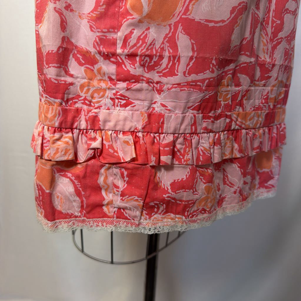 A pink & peach floral mod dress on a dress form in front of a white wall.