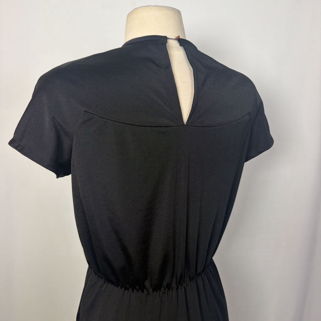 A black short-sleeve top with a gathered, pleated front bodice and a wide crew neckline, displayed on a beige mannequin torso against a light gray background.