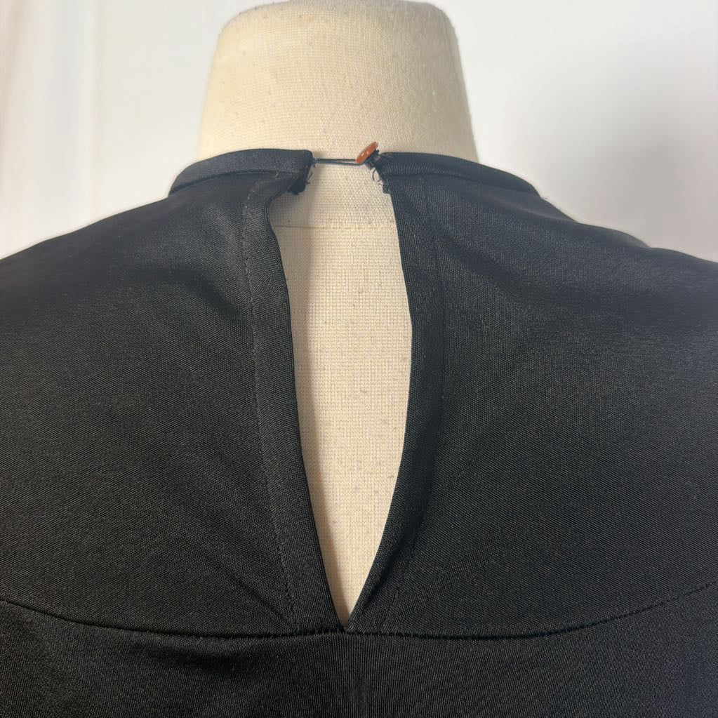 Close-up of the back neckline of a black top displayed on a cream fabric mannequin torso, showing a deep V-shaped keyhole opening with a small pin closure at the top.