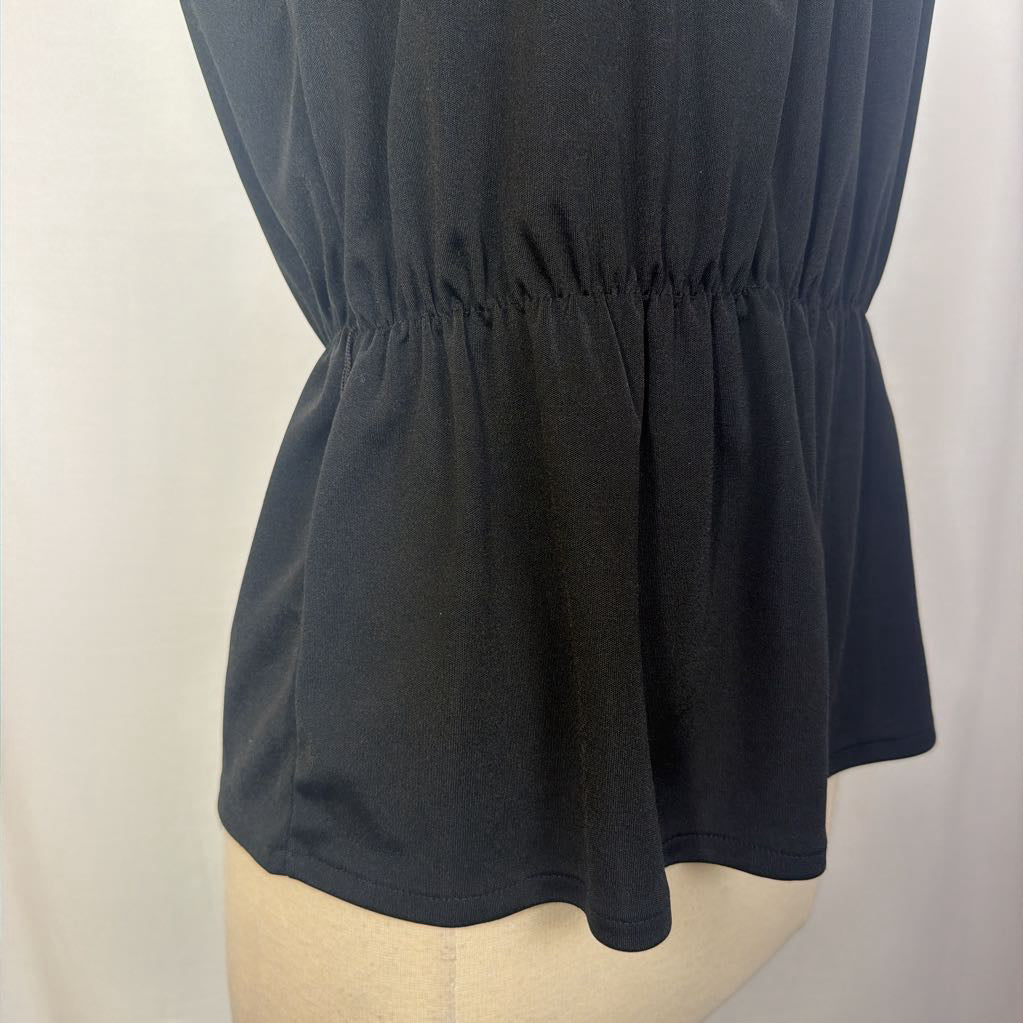 Close-up of a black peplum-style top or dress section displayed on a beige dress form against a light neutral background.