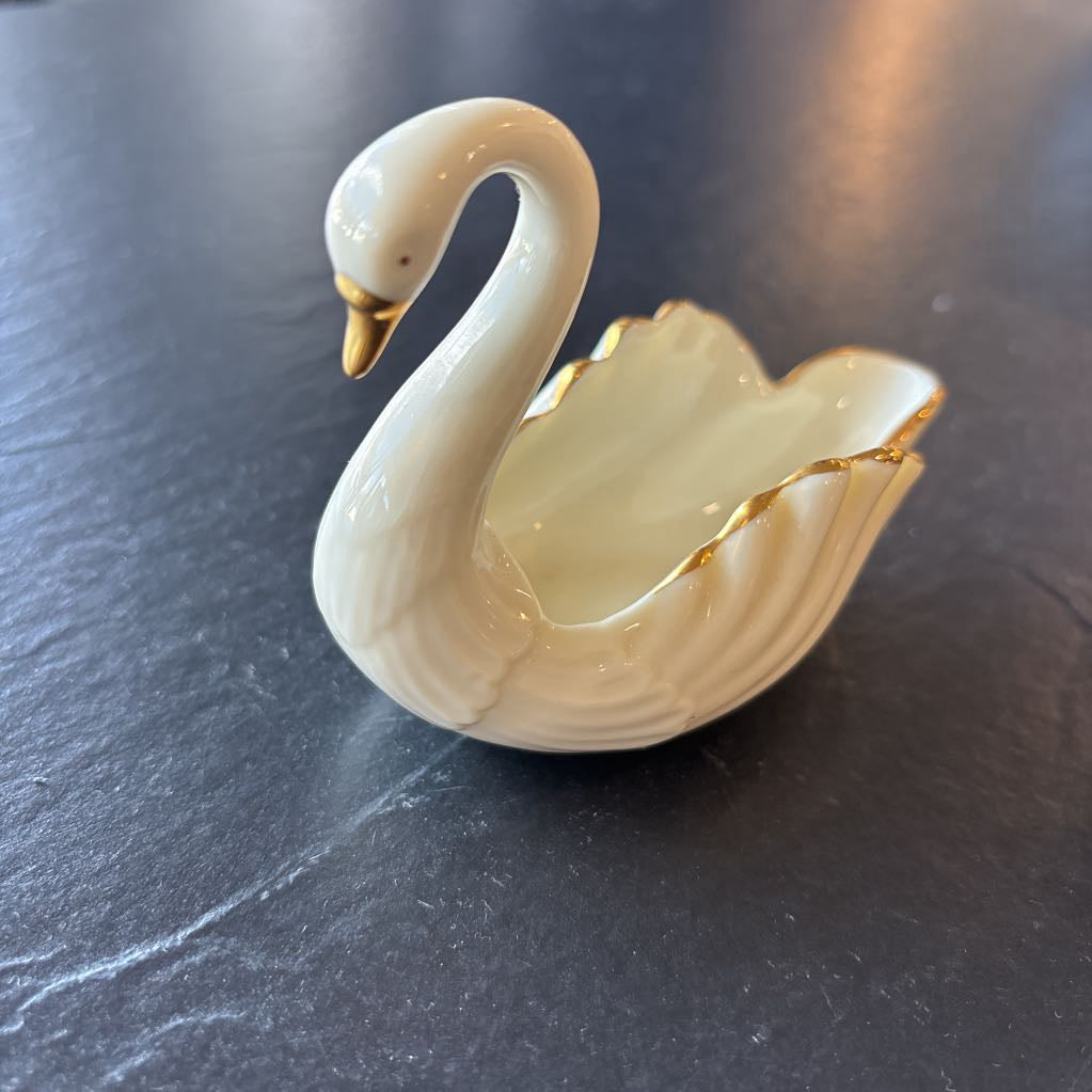 A small ceramic white swan figurine with gold trim on the wings and beak on a dark surface.