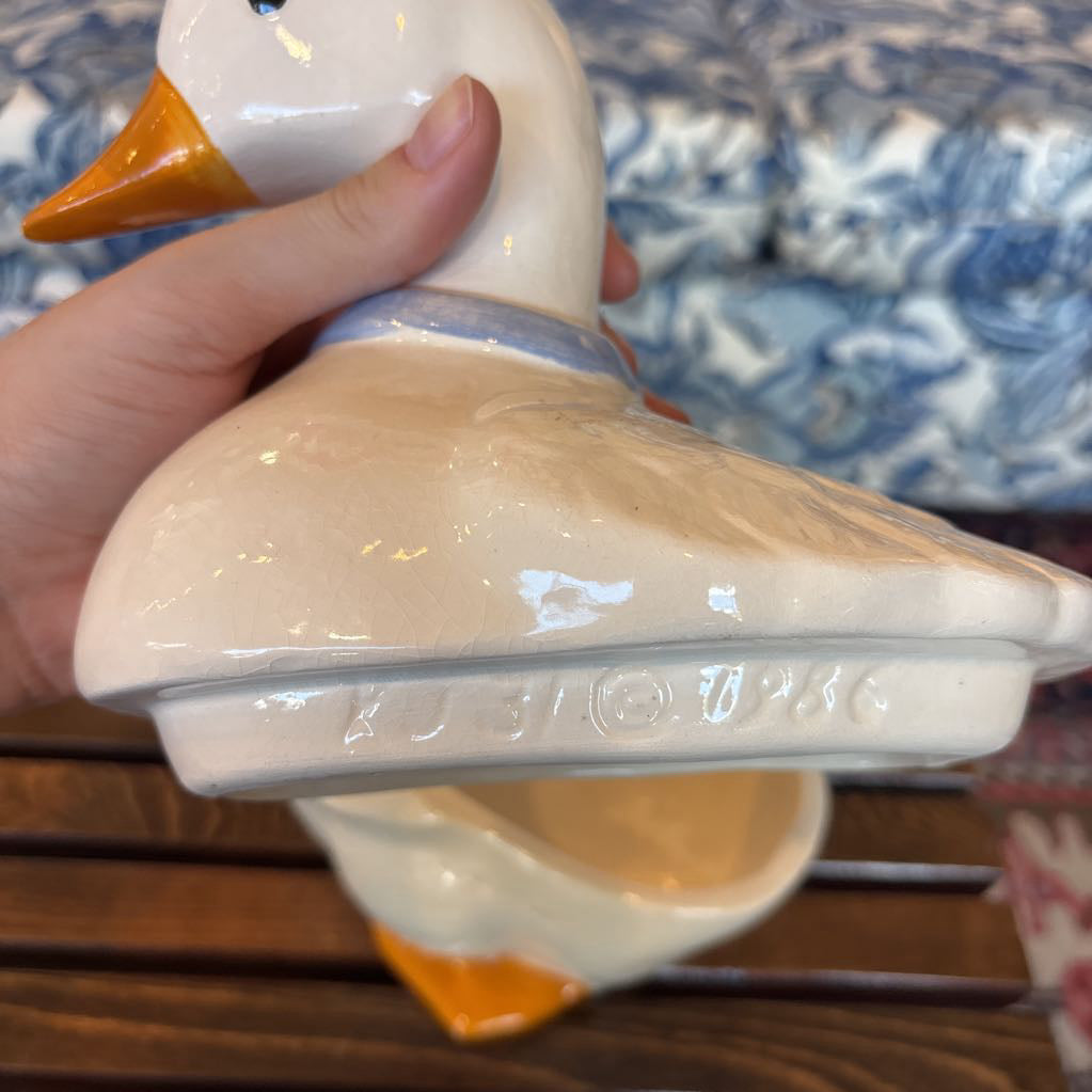 A hand holding the top of a duck shaped cookie jar showing the branding stamps along the lip of the lid.