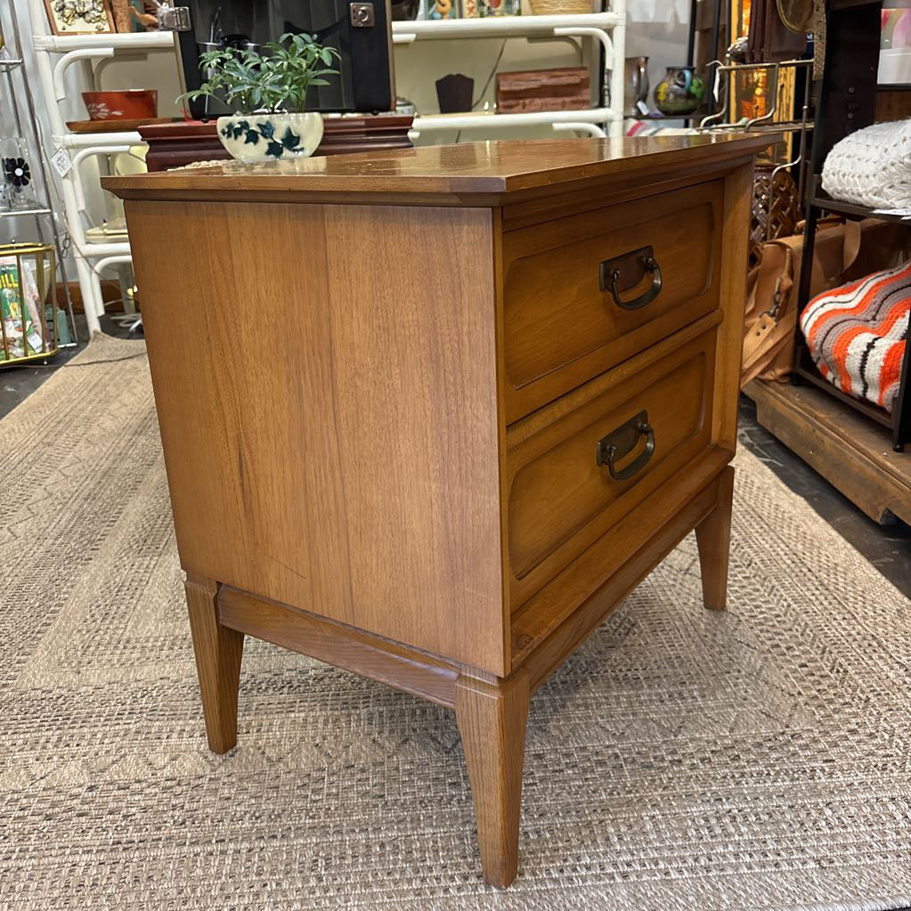 A wooden nightstand with drawers in a store setting.