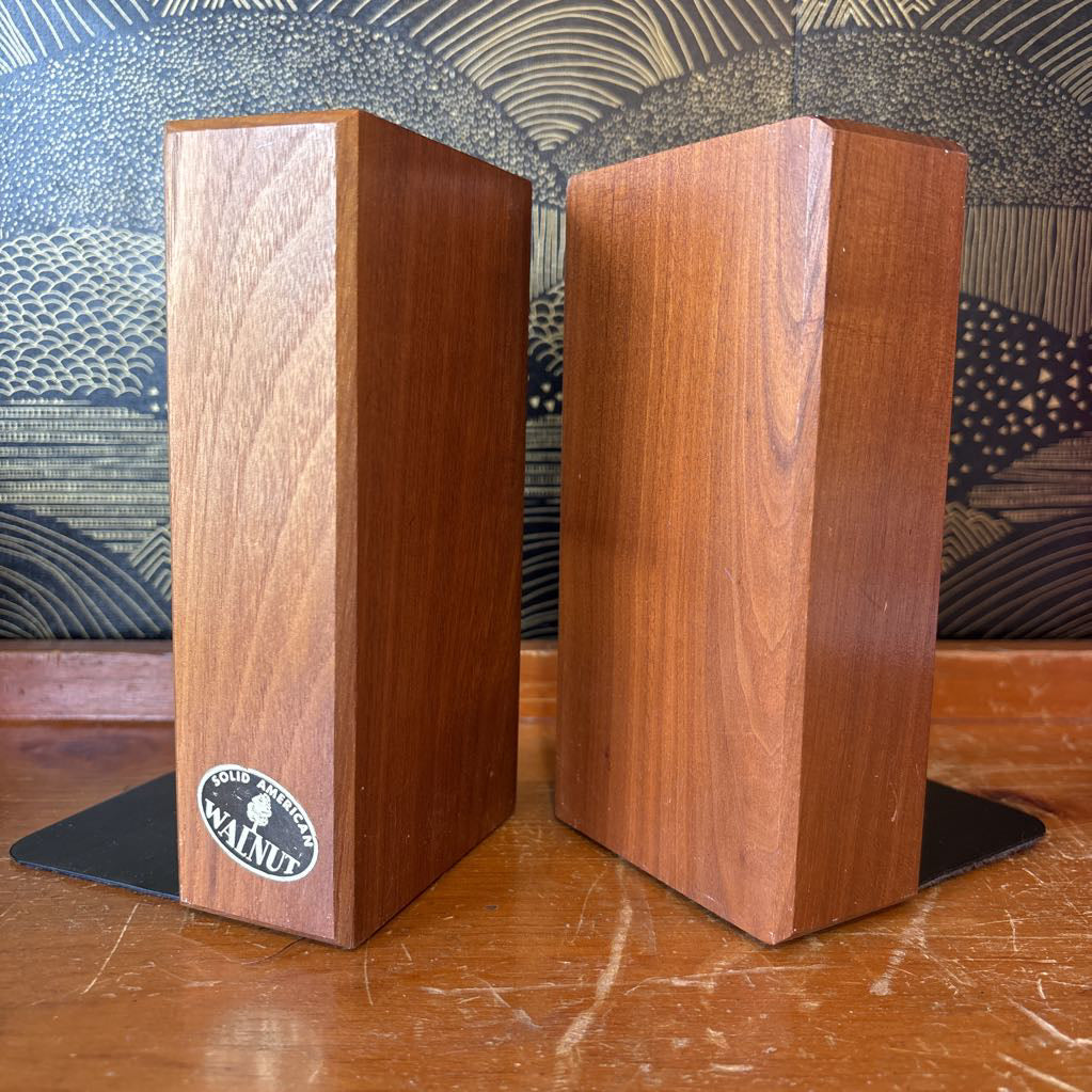Two wooden bookends sitting on a wooden surface in front of a black and gold wallpaper.