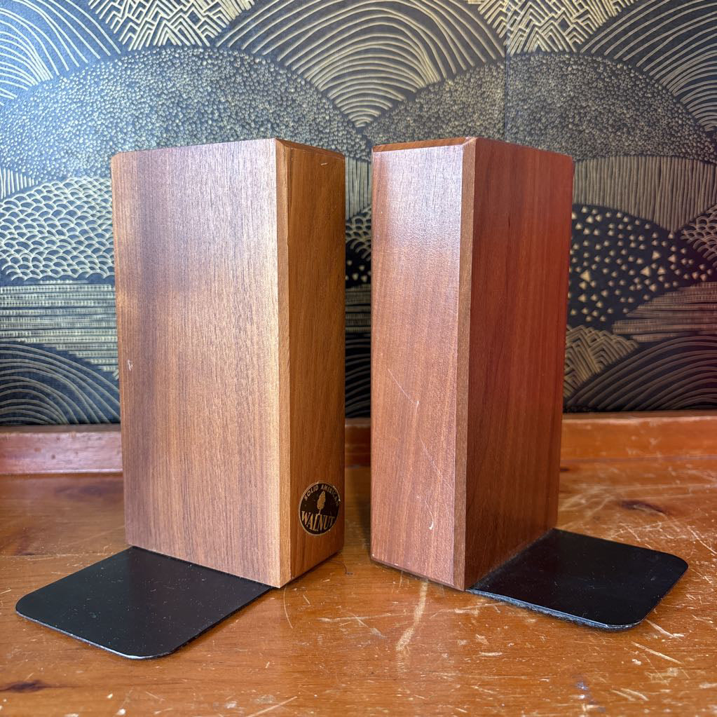 Two wooden bookends sitting on a wooden surface in front of a black and gold wallpaper.