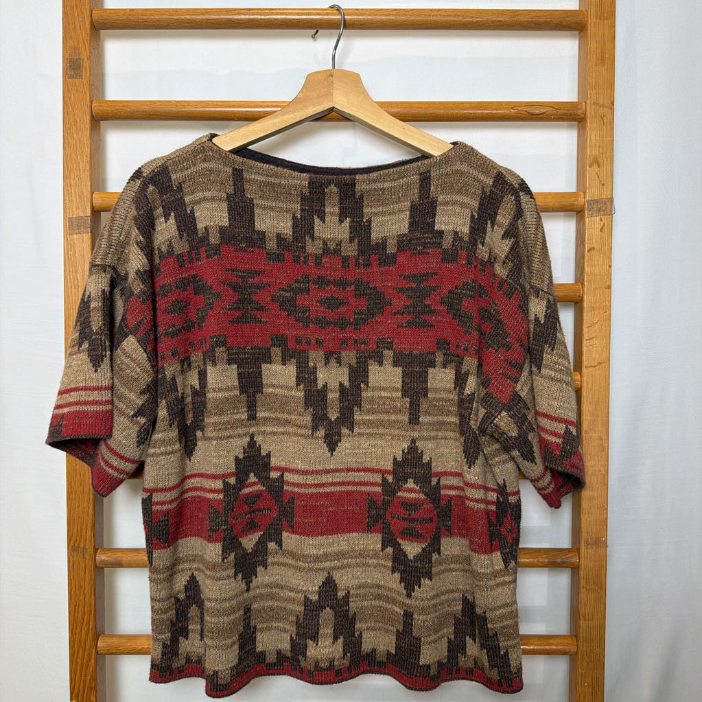 A short sleeve sweater with a tapestry design on a wooden rack.