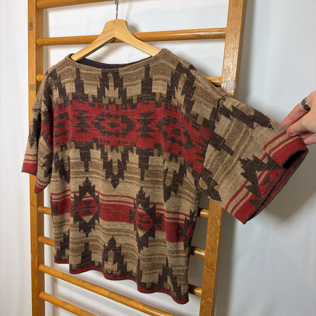 A short sleeve sweater with a tapestry design on a wooden rack.