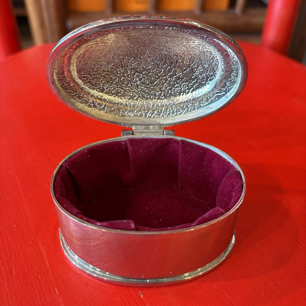 A silver jewelry box with a velvet interior on a red surface.