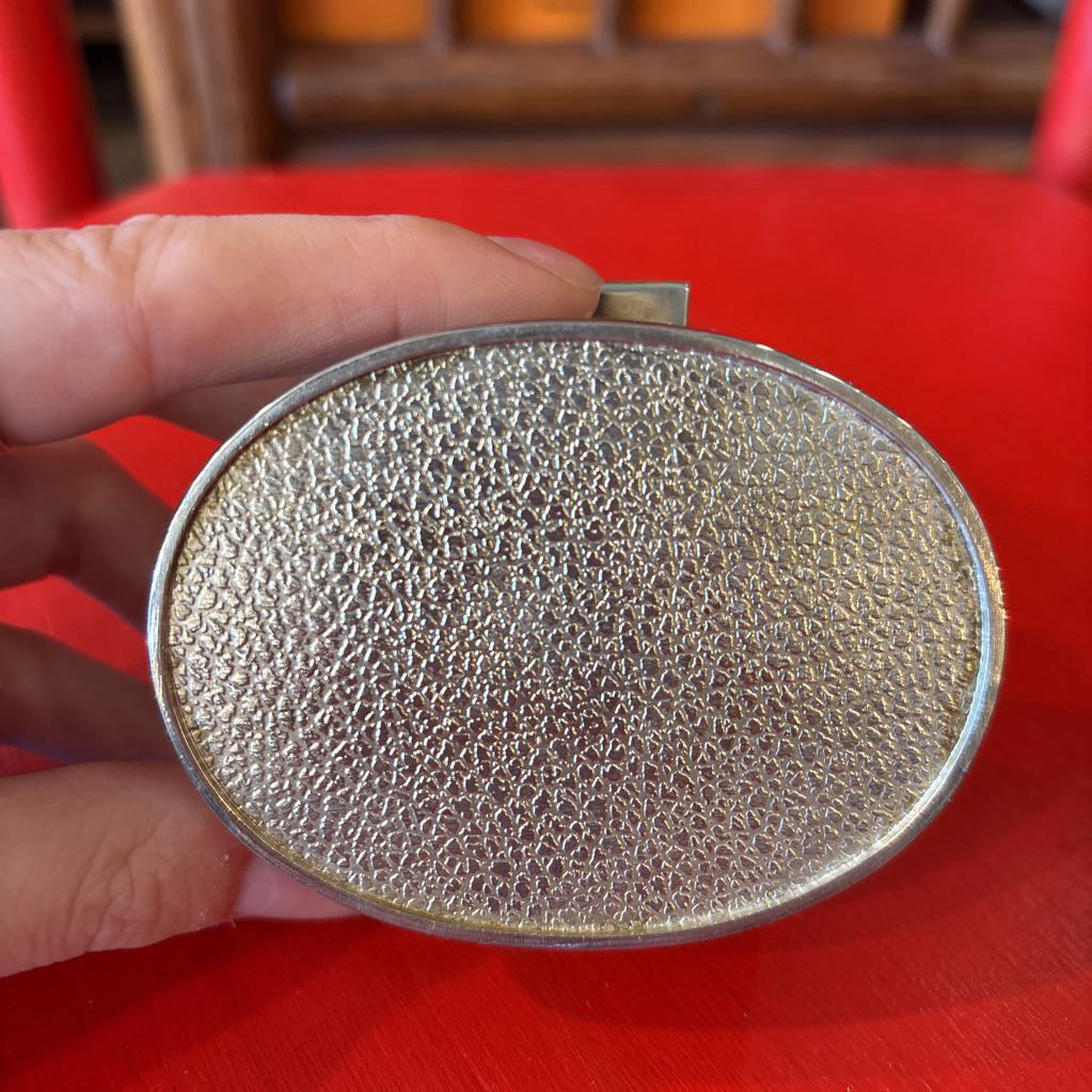 A silver jewelry box being held by a hand over a red surface.