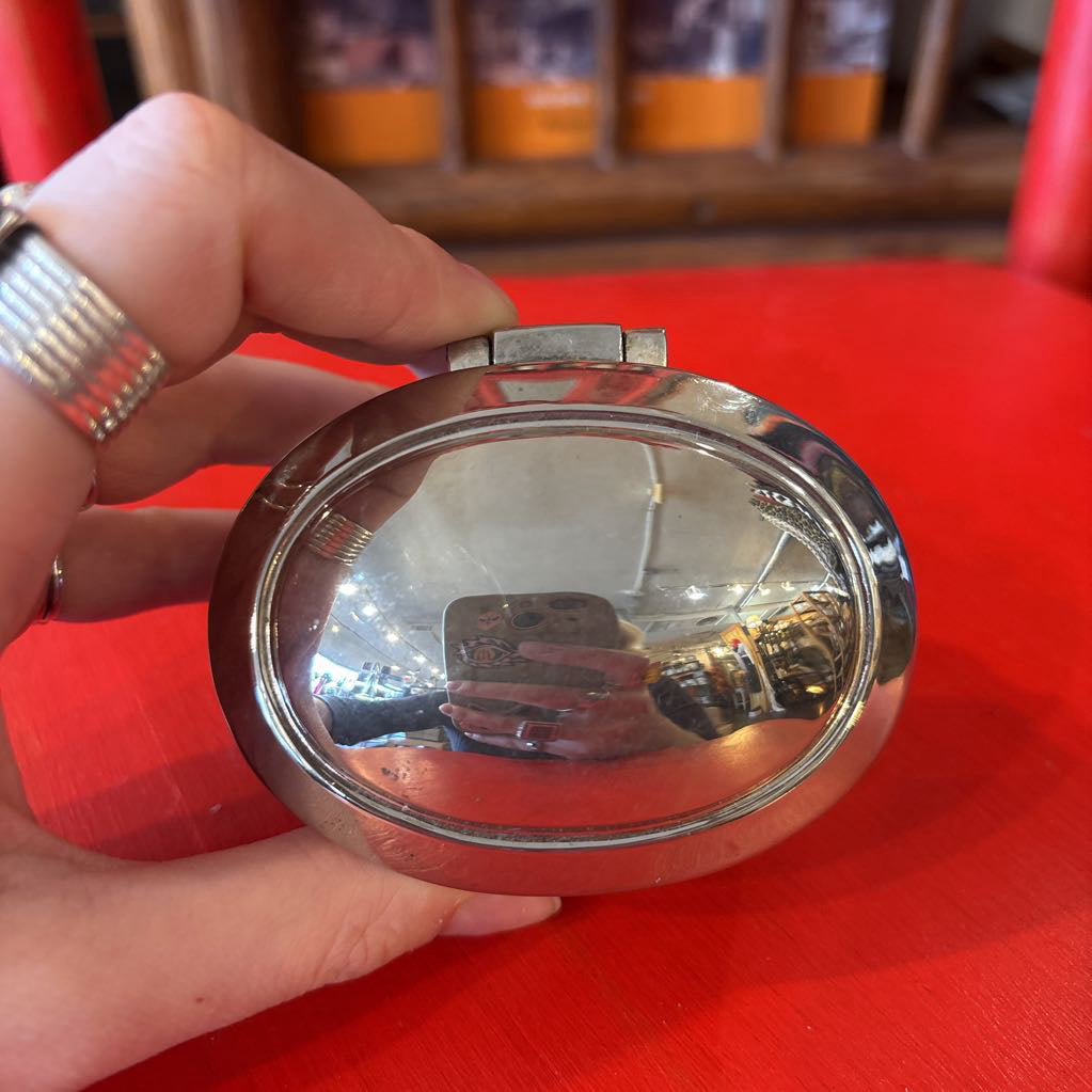 A silver jewelry box being held by a hand over a red surface.