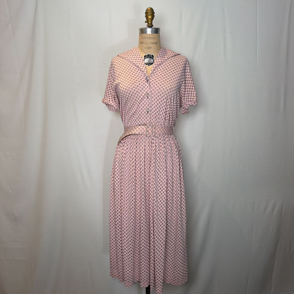 A light pink dress with cuffed sleeves and a belted waist on a mannequin in front of a white wall.