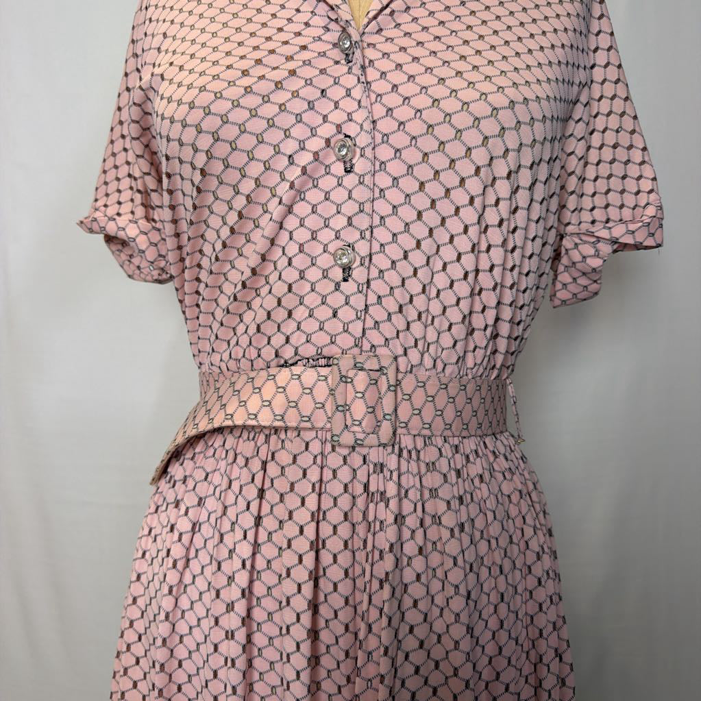 A light pink dress with cuffed sleeves and a belted waist on a mannequin in front of a white wall.