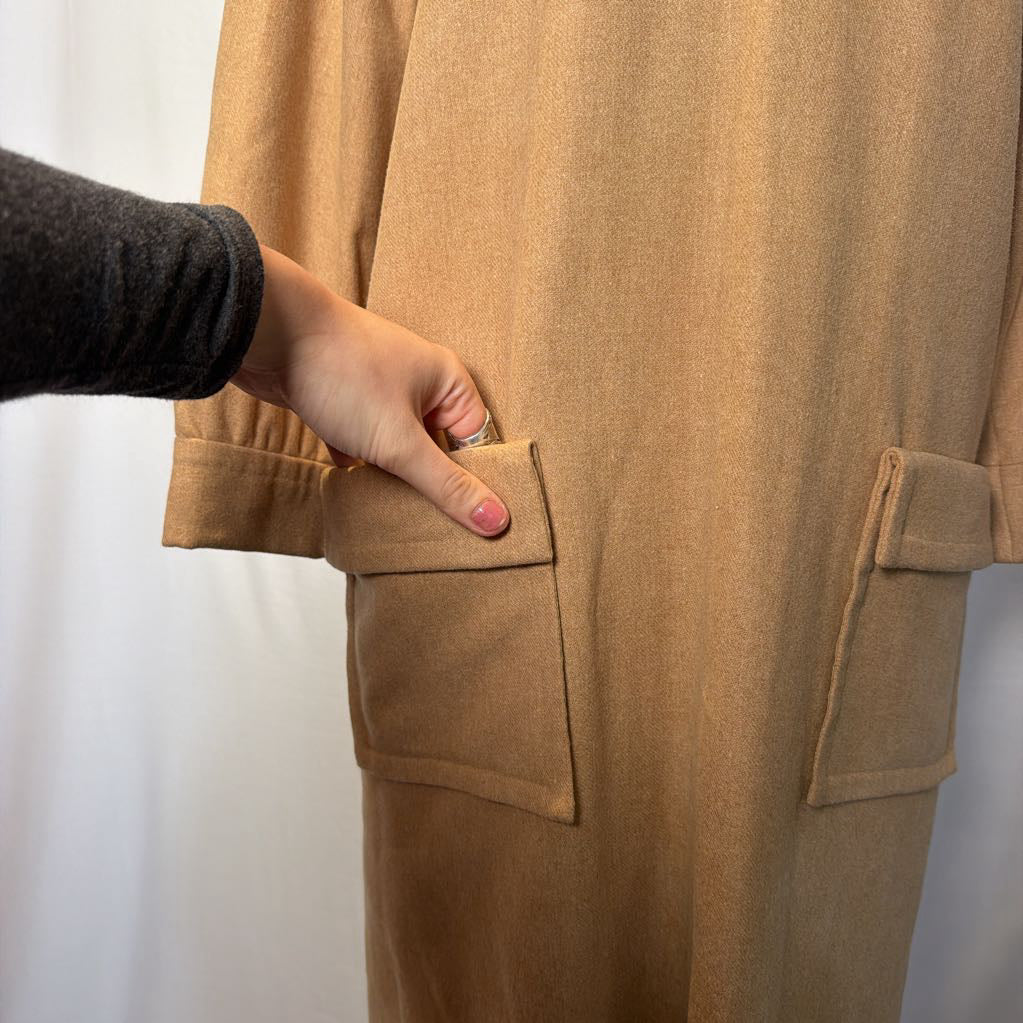 A long sleeve tan wool dress on a mannequin in front of a white wall.